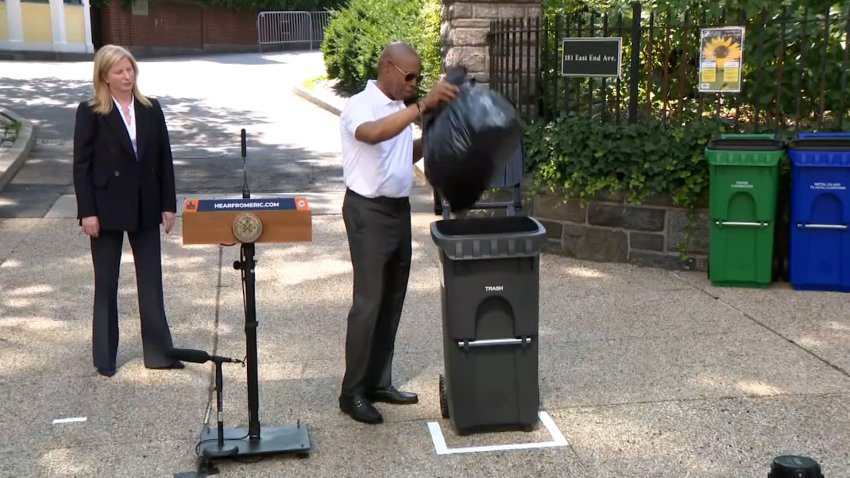 Mayor Eric Adams throws a bag of trash into a bin at a press conference