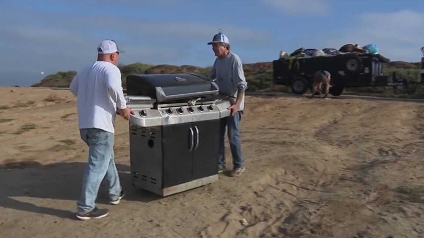 Retired National City Fire Captain Derek Jones (left) and a friend (right) haul a grill that was left on Fiesta Island, July 5, 2024.