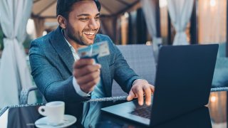 Smiling businessman with laptop and credit card in a restaurant in the evening