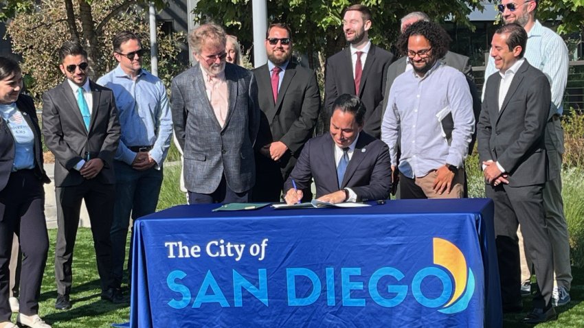 San Diego Mayor signs new law while stakeholders stand behind him.