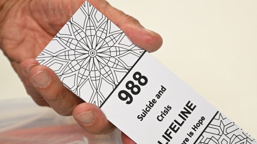 A bookmark for children with the 988 suicide and crisis lifeline emergency telephone number is displayed by Lance Neiberger, a volunteer with the Natrona County Suicide Prevention Task Force, while they speak about mental health and suicide awareness in Casper, Wyoming on August 14, 2022.