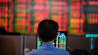 A Thai investor checks an electronic board showing stock prices.