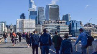 People walk along London Bridge past the City of London skyline.