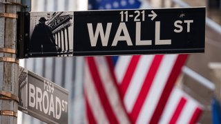 U.S. Flags on the front of the New York Stock Exchange hang behind the street signs making the corner of Wall and Broad Streets in the center of the financial district on October 24, 2024 in New York City. 