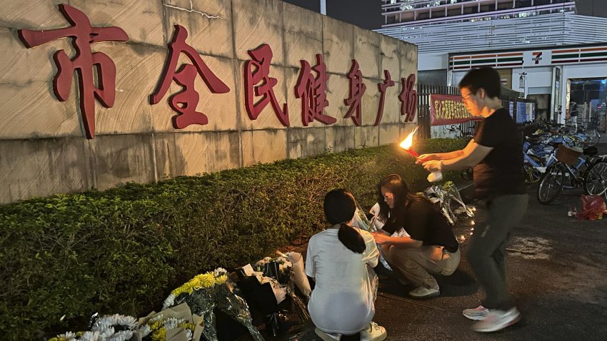 A woman lights a candle as offering near flowers placed outside the "Zhuhai People's Fitness Plaza"