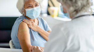 A womant holds up her sleeve and smiles as she looks up at her doctor after receiving a vaccination in this undated image.