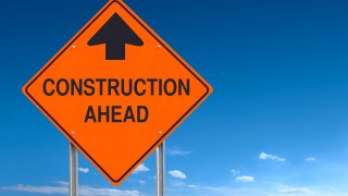 An orange "Construction Ahead" sign is displayed with a blue sky in the background in this undated image.