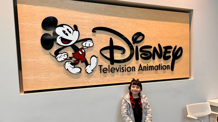 Girl stands in front of a Diseny sign.