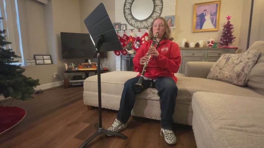 Girl in red jacket plays clarinet while sitting on a couch