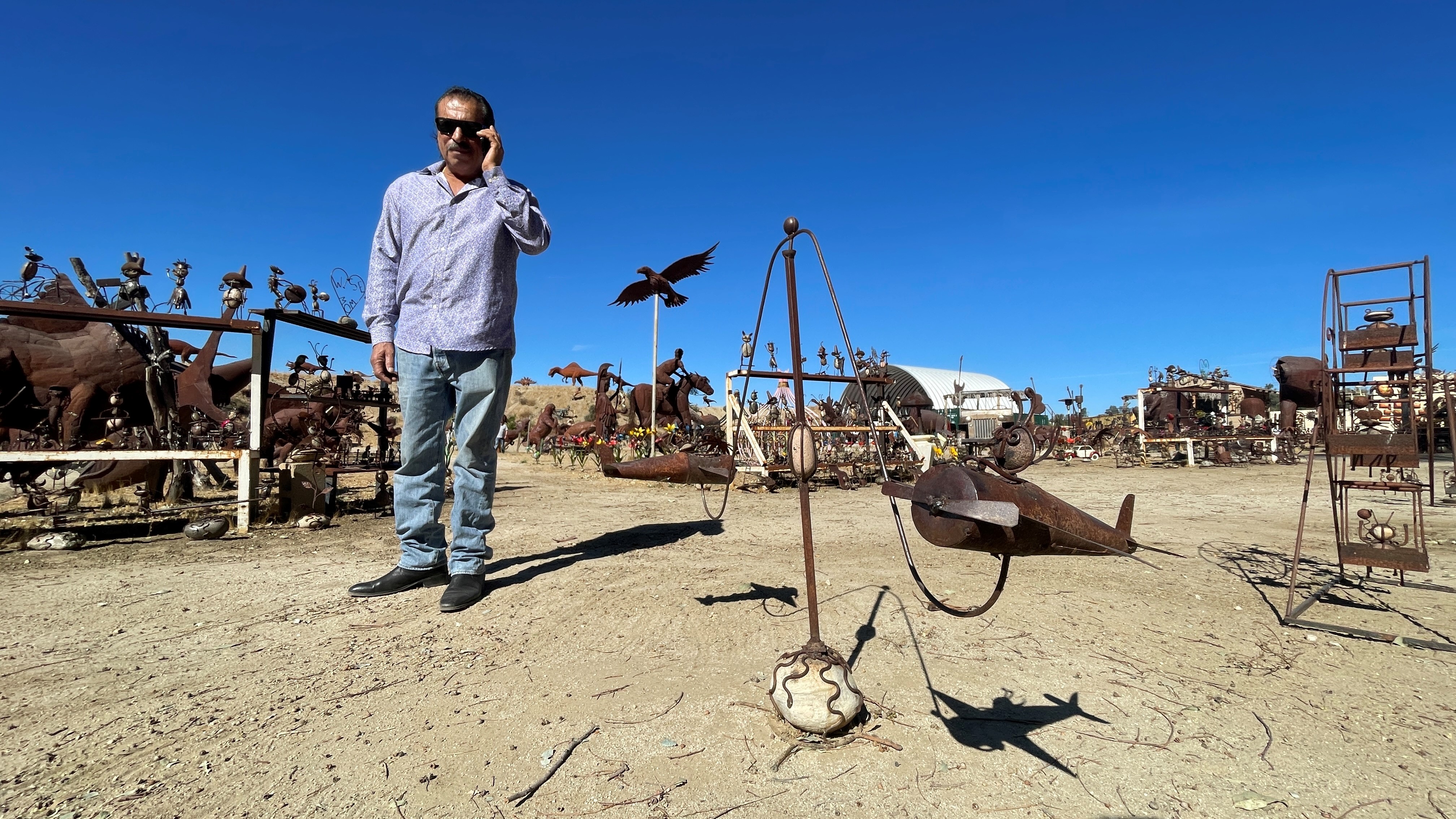 Man talks on the phone while standing near metal sculptures.