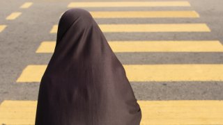File. A shrouded muslim lady with hijab walks across the zebra crossing.