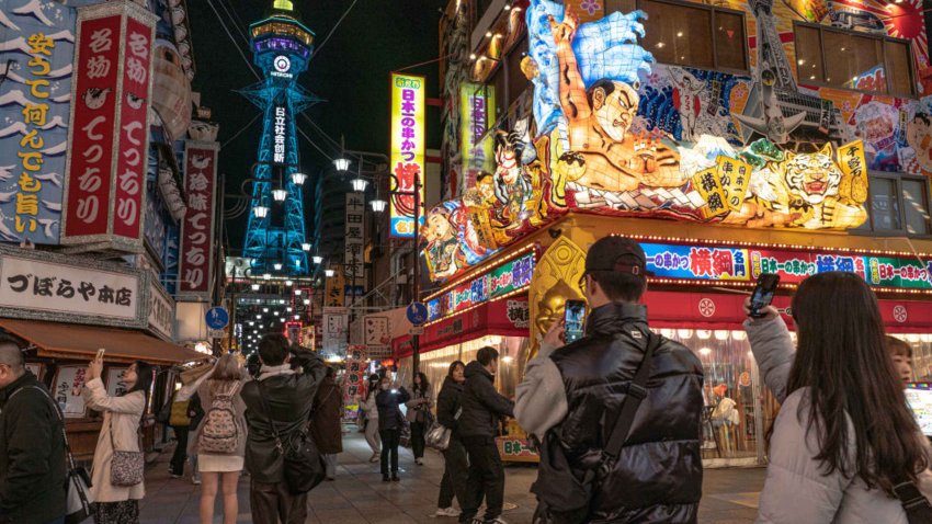 Tourists take photos in Shinsekai with Tsutenkaku tower in sight in Osaka, Japan, on December 12, 2024. 