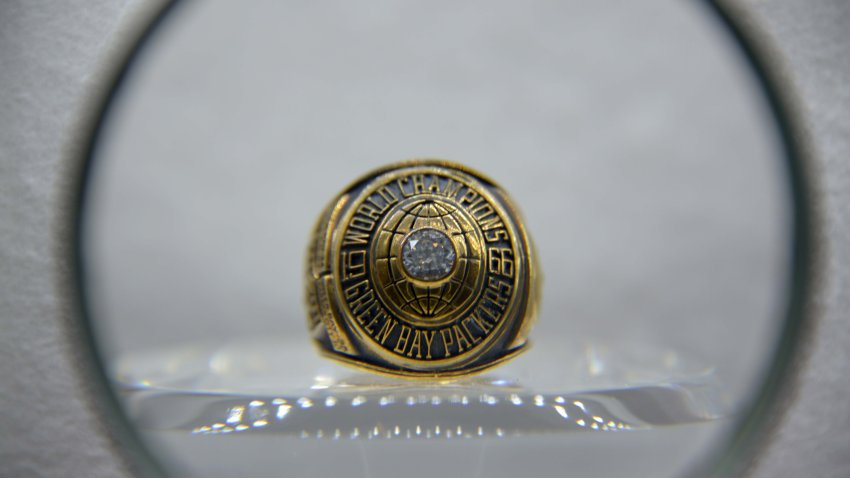 A Packer's Super Bowl championship ring from Super Bowl I is displayed through a circular lens. The ring is engraved with the words "World Champions," "1966" and "Green Bay Packers." It has a single diamond in the middle.