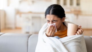 Cold And Flu Symptoms . Sick indian woman covered in blanket blowing nose