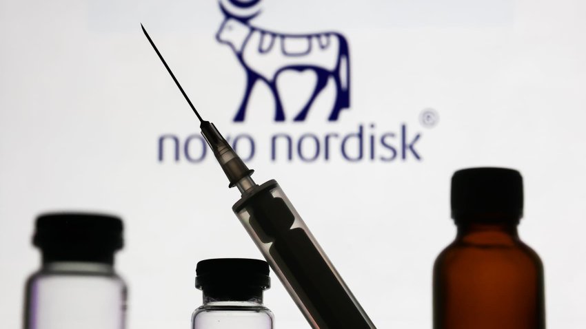 Medical bottles and syringe are seen with Novo Nordisk logo displayed on a screen in the background.