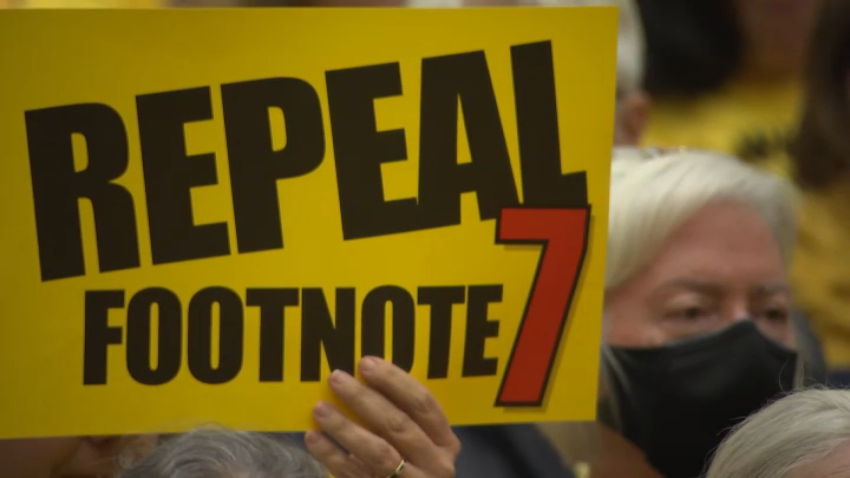 A person holds a sign that reads, "Repeal Footnote 7."