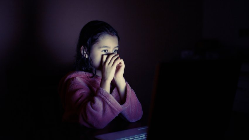 Girl using laptop in dark room, face in surprise.