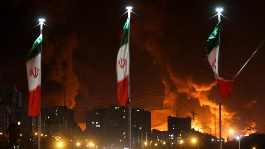 Iranian flags fly as fire and smoke from an Israeli attack on Sharan Oil depot rise, following Israeli strikes on Iran, in Tehran, Iran, June 15, 2025.
