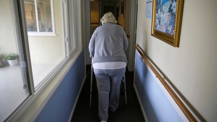 FILE – A woman uses a walker as she heads to her room at a senior care home in Calistoga, Calif., on Dec. 5, 2019.