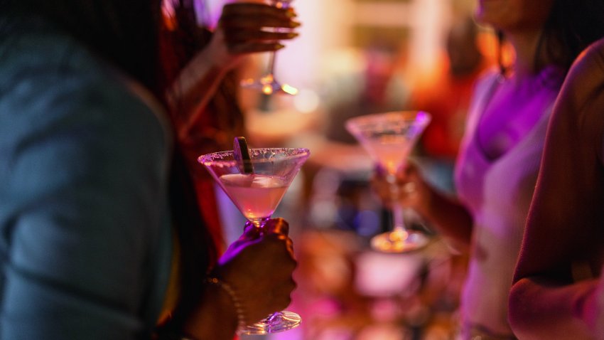 Close-up of a martini glass held by a female at a bar with purple lighting. Delicious summer cocktail.