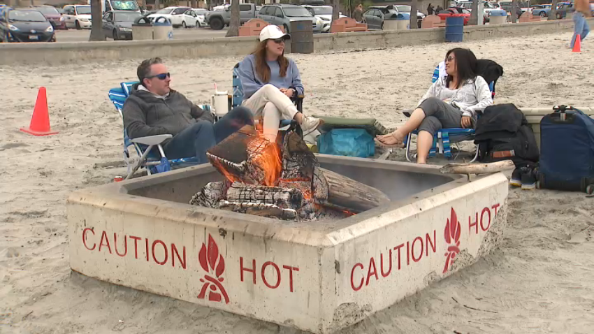 Three people sitting around a fire pit at the beach in San Diego on June 5, 2025.