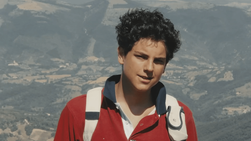 Photo of Carlo Acutis with landscape behind him