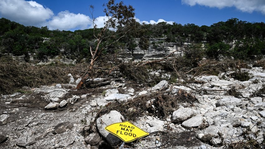 A traffic sign reading "Road may flood" lies on the ground near the Guadalupe River in Hunt, Texas, on July 8, 2025.