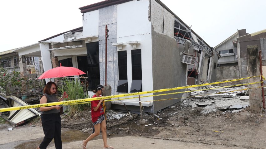 Two women walk past a damaged house after a strong earthquake in Davao City, southern Philippines on Friday Oct. 10, 2025.