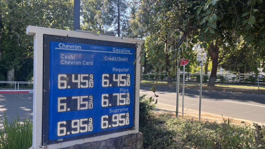 A blue billboard outdoors lists gas prices, with regular selling for 6.45 a gallon.